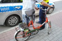 Zdjęcie kolorowe: Na tle radiowozu stoi rowerzysta a obok niego policjant.