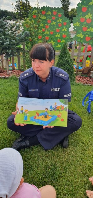 Zdjęcie kolorowe. Policjantka siedząca na trawie trzyma w rękach książeczkę