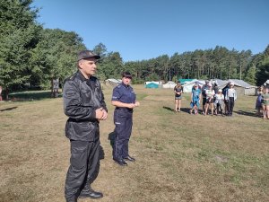 Zdjęcie kolorowe. Strażak wraz z policjantką na spotkaniu z uczestnikami obozu.