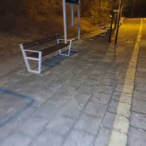 Zdjęcie kolorowe. Zdjęcie zrobione nocą. Na chodniku porozrzucane szkło z tablicy informacyjnej z boku stoi ławka i słup z nazwą miejscowości Przeradź