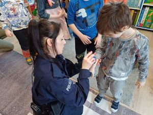 Zdjęcie kolorowe. Policjantka przybija na rączki dzieci pamiątkowe pamiątki