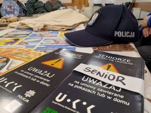 Zdjęcie kolorowe. Policyjna czapka lezy na ulotkach o tematyce bezpieczeństwa seniorów