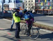 Zdjęcie kolorowe. Policjantka wręcza na chodniku rowerzyście element odblaskowy